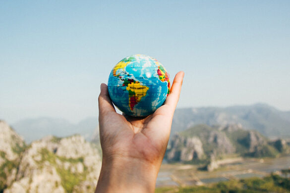 Stock photo of a person holding a small globe while looking out over an expansive view, symbolic of Earth Week.